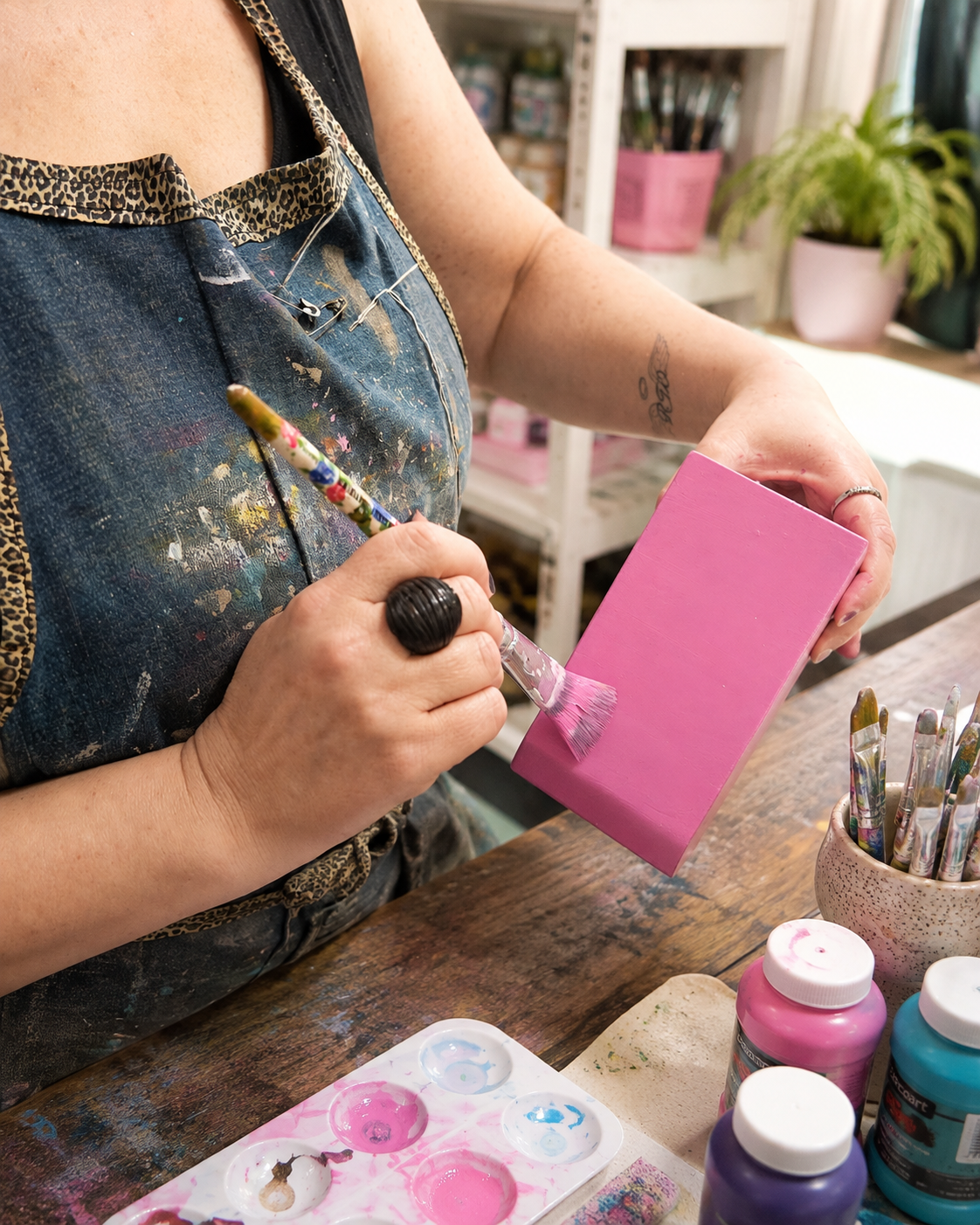 Mãos pintando uma peça rosa no Ateliê