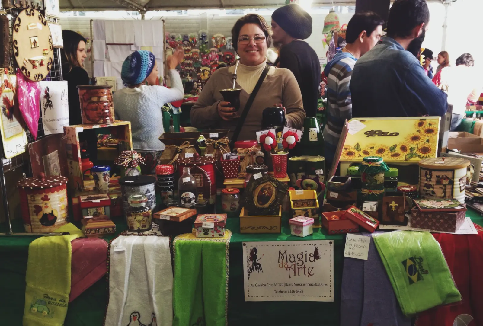 Julici em uma feira de artesanato, diante da banca do Ateliê Magia da Arte