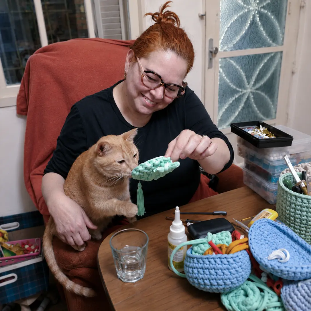 Julici criando uma peça de crochê acompanhada por um dos gatos da família